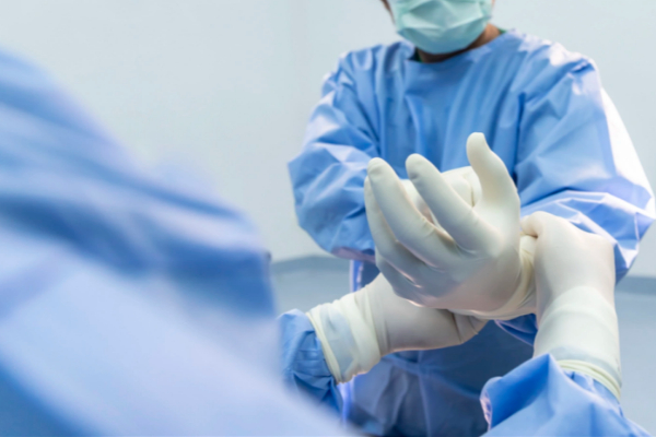 A medical professional in a surgical gown puts on sterile gloves.