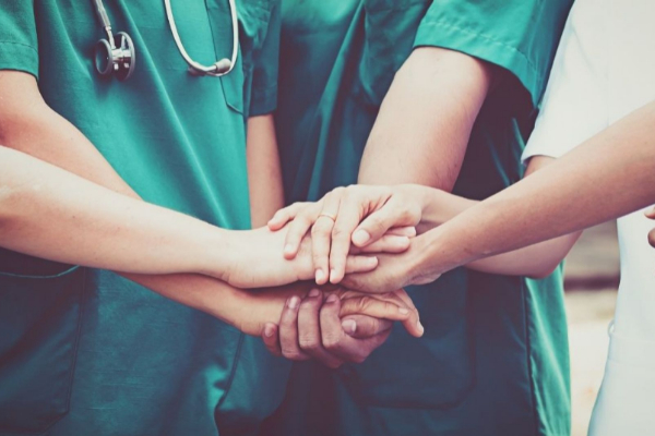 Medical professionals in green uniforms place their hands together in a show of unity and teamwork.