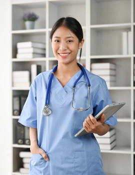 Medical professional in blue scrubs holds a tablet and smiles in front of shelves with books and decor.