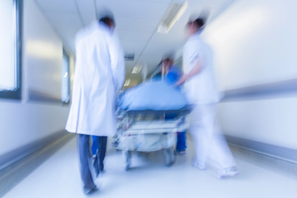 Blurred image of medical staff in white coats quickly wheeling a patient on a stretcher down a hospital corridor.